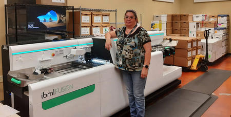 An image showing a large ibml fusion scanner with IDS Pueblo Scanning Manager Sandy Justus standing in front of